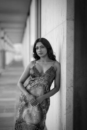 A black and white portrait of someone wearing a glamorous sequined evening gown while leaning against a column.
