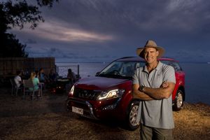 A red car and Cricketer Matthew Hayden set against a dramatic sunset sky and rural landscape with a moody atmosphere.