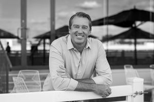 Glenn McGrath standing at a white picket fence in front of the pavilion at the Wangaratta turf club.