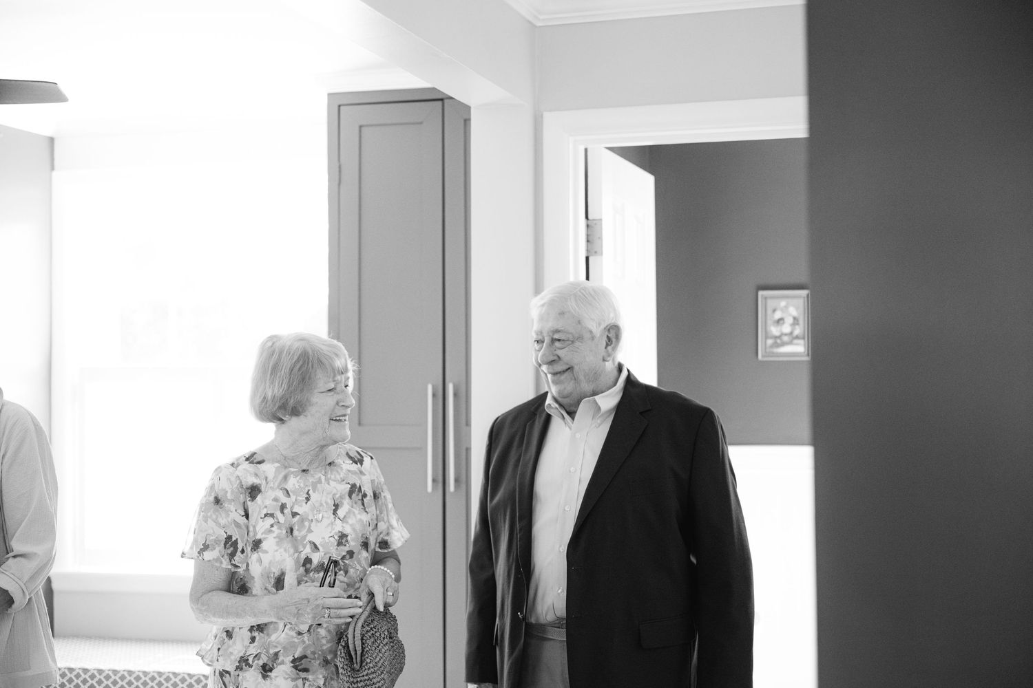 People dressed in formal attire walk through a bright hallway interior during a wedding event.