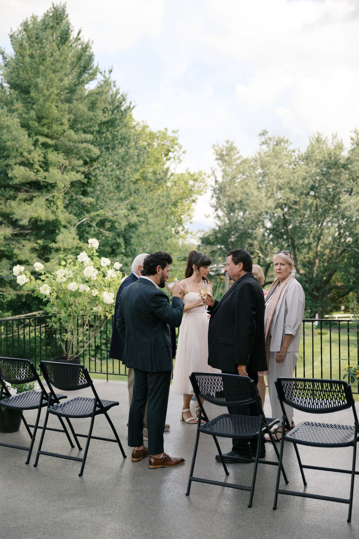 Small outdoor wedding ceremony on a patio with folding chairs and lush greenery in the background.