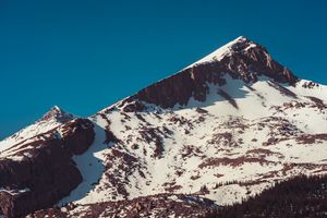 Snow-covered mountain peak rises against deep blue sky with rugged rocky terrain visible.