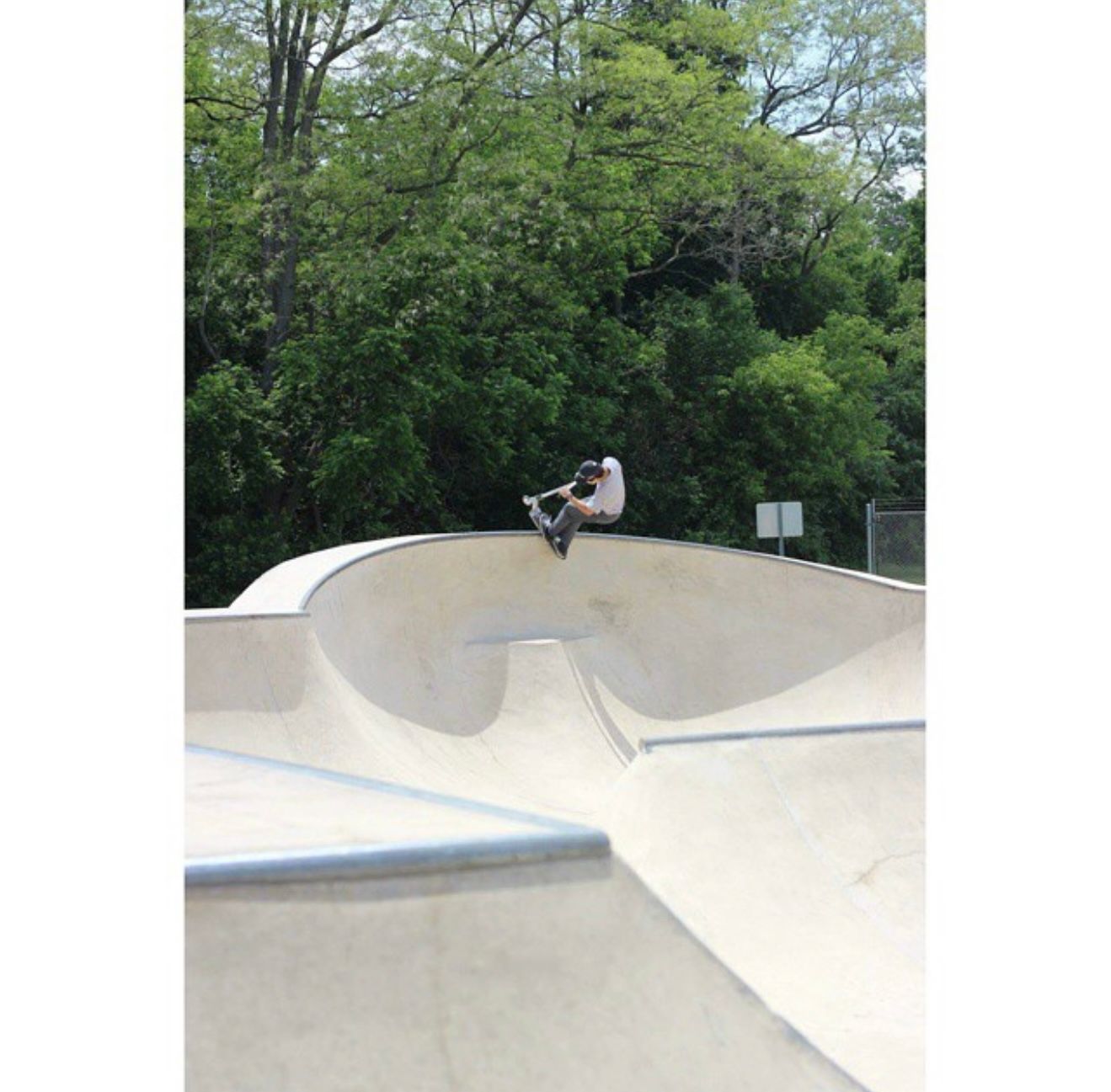 Skateboarder performs an aerial maneuver off a curved white ramp at an outdoor concrete skate park.