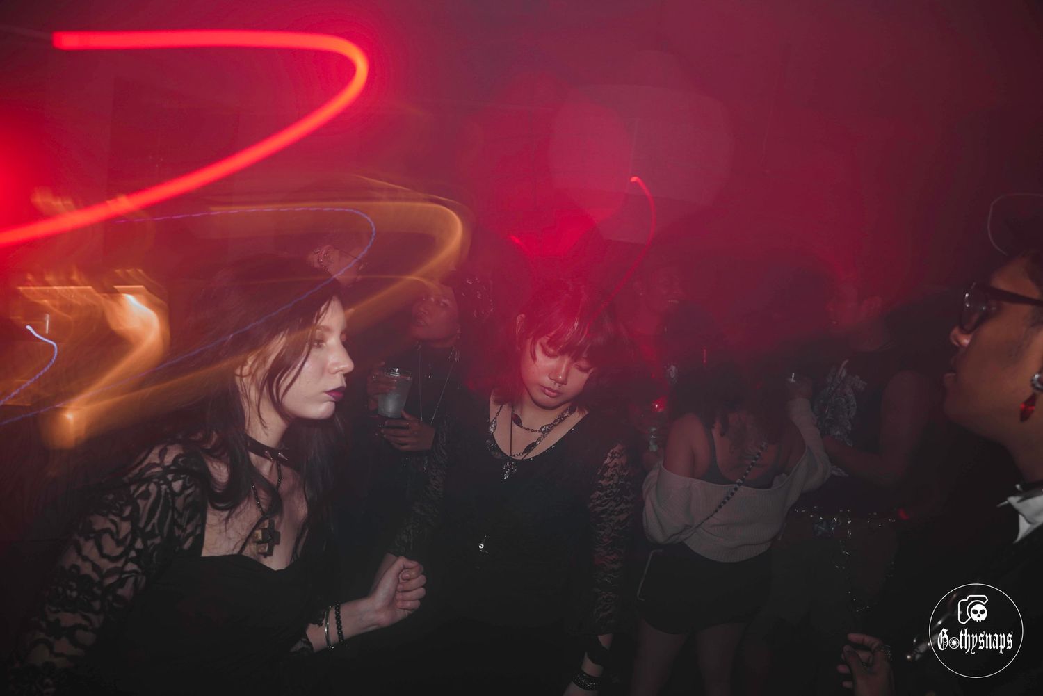 People dancing at a crowded nightclub with red neon lighting and smoky atmosphere.