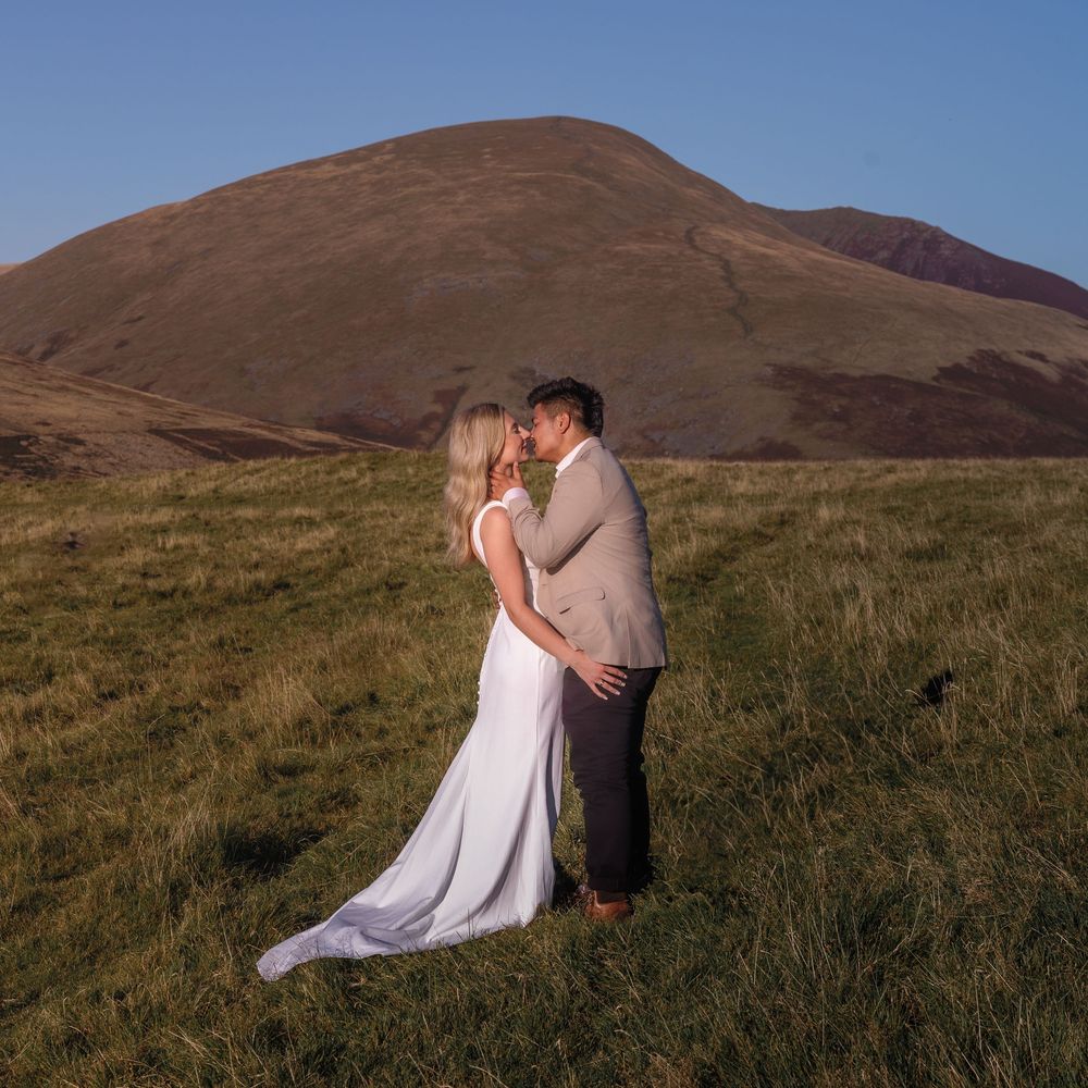 Couple in elegant attire embracing on grassy hillside with mountains in sunset background, captured in sequential shots.