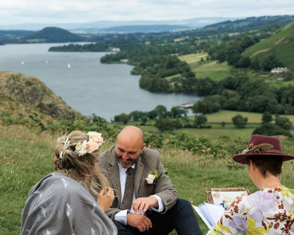 A scenic outdoor proposal takes place along a cliffside path overlooking a beautiful lake and rolling hills.
