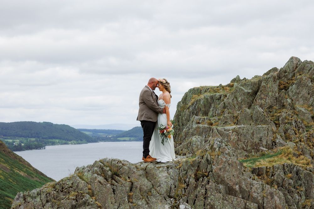 Two figures embrace on a dramatic cliff edge overlooking a misty lake and mountain landscape.