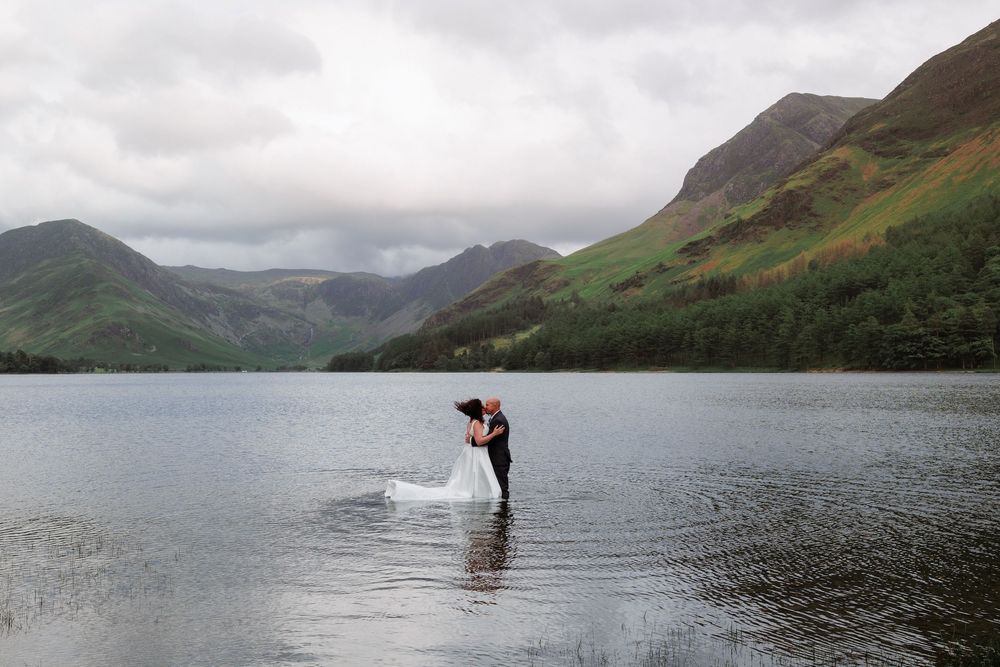Person stands in a lake with mountains of the Scottish Highlands creating a dramatic backdrop under cloudy skies.