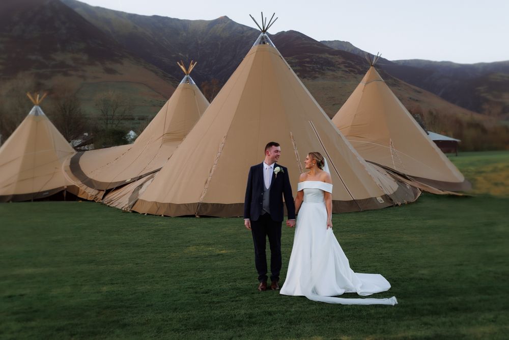 Traditional tipi-style wedding venue tents set up in a scenic green valley with rolling hills in the background.