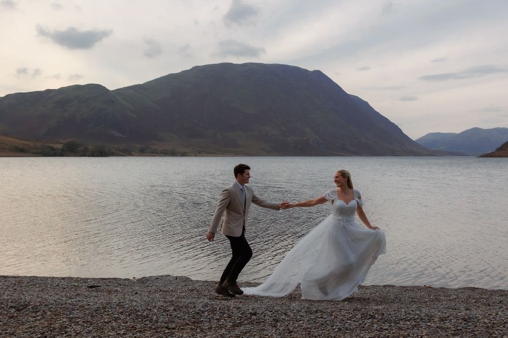 A couple dances together on a rocky beach with mountains and a lake creating a romantic Scottish Highland backdrop.