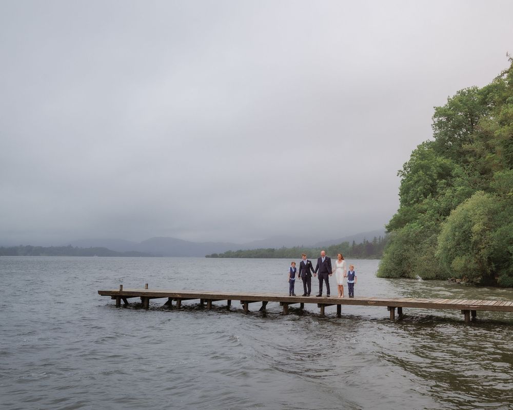 People standing on a wooden dock extending into a misty lake surrounded by trees on a cloudy day.