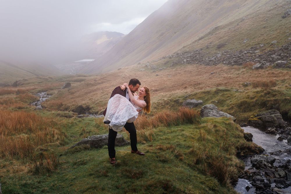 Two people embrace in a romantic moment along a misty mountainside stream in autumn.