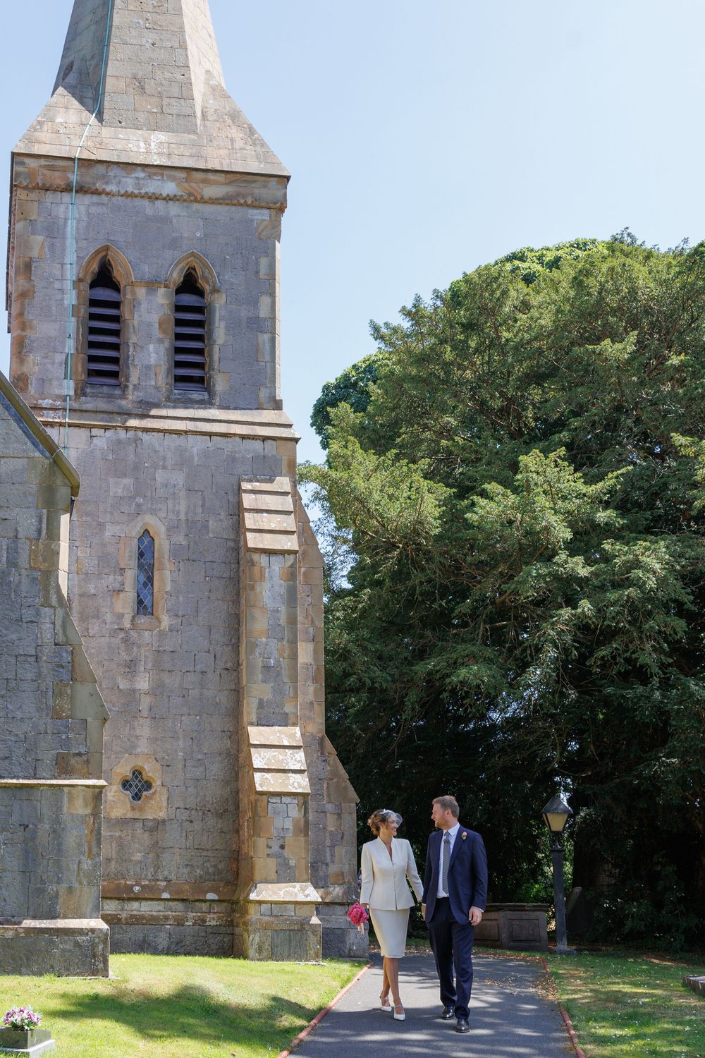 Three historic stone church towers with pointed gothic windows stand among green trees on a sunny day.
