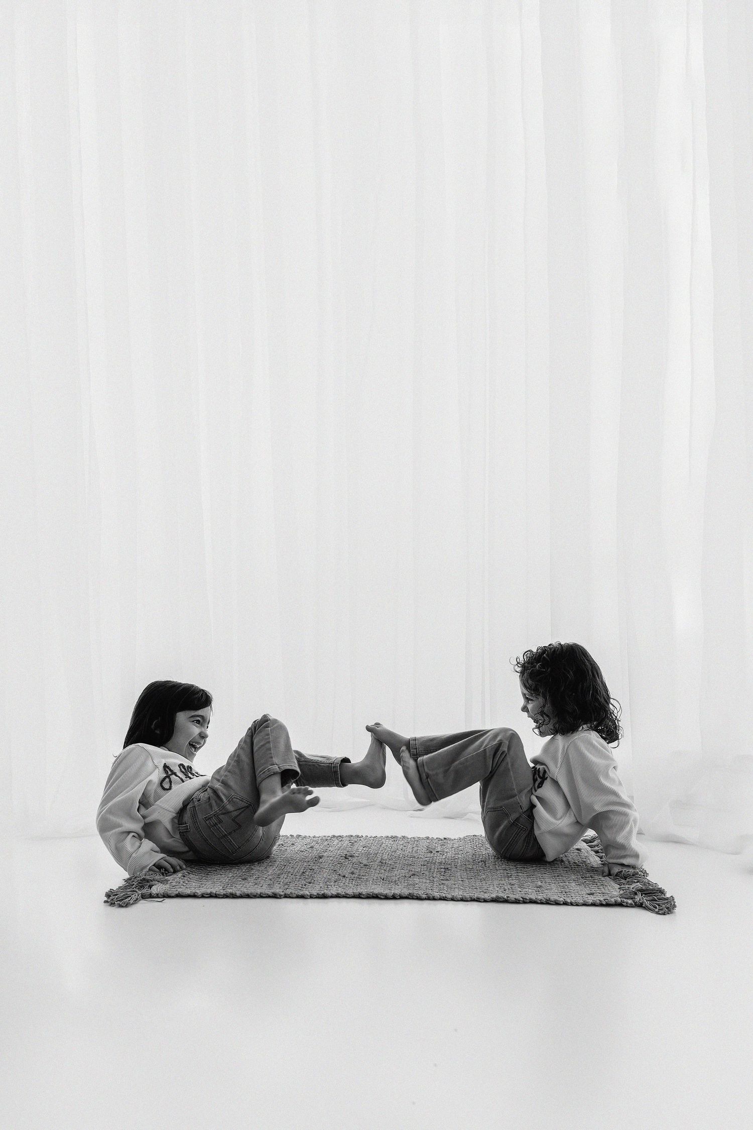 Two people lying down facing each other with their feet touching on the floor in a minimalist black and white setting.
