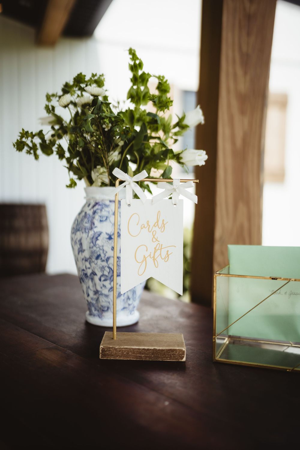 A blue and white pottery vase with white flowers and greenery next to a card holder on a dark wooden surface.