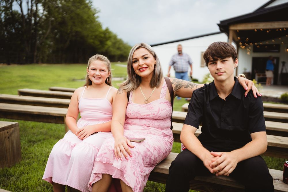 Three people sitting together on outdoor wooden steps in formal attire on a sunny day.