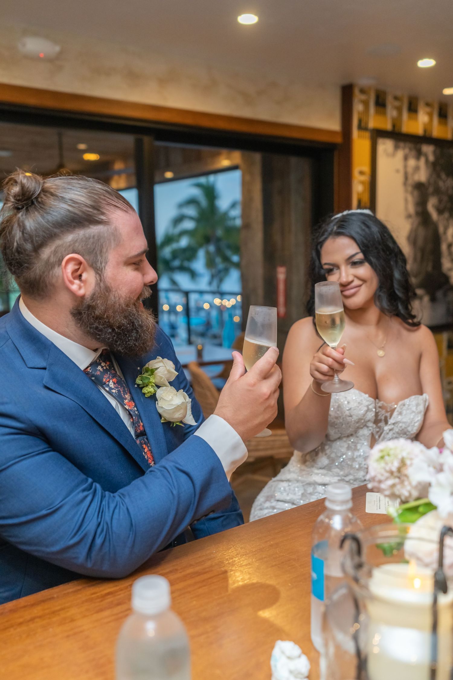 Wedding couple toasting at a bar with tropical scenery in the background.