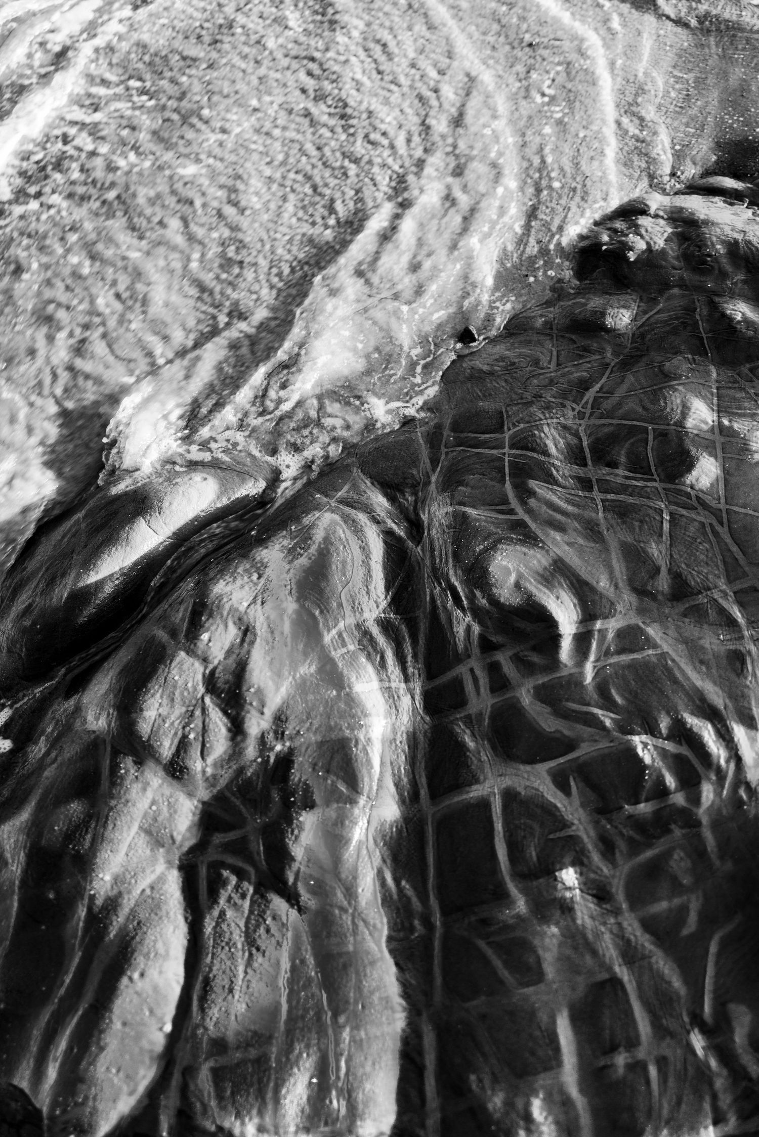 Black and white close-up of wet rocks with light reflecting off shallow water creating abstract patterns.