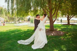Wedding celebration group arranged around willow tree with white dress trailing behind.
