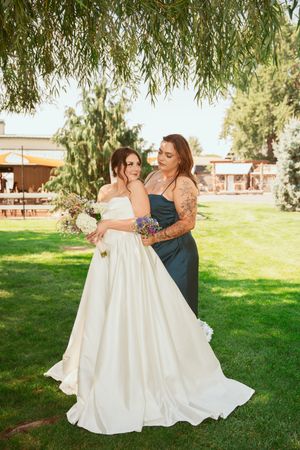 A couple dances and embraces on a grassy lawn with willow trees in the background during their wedding celebration.