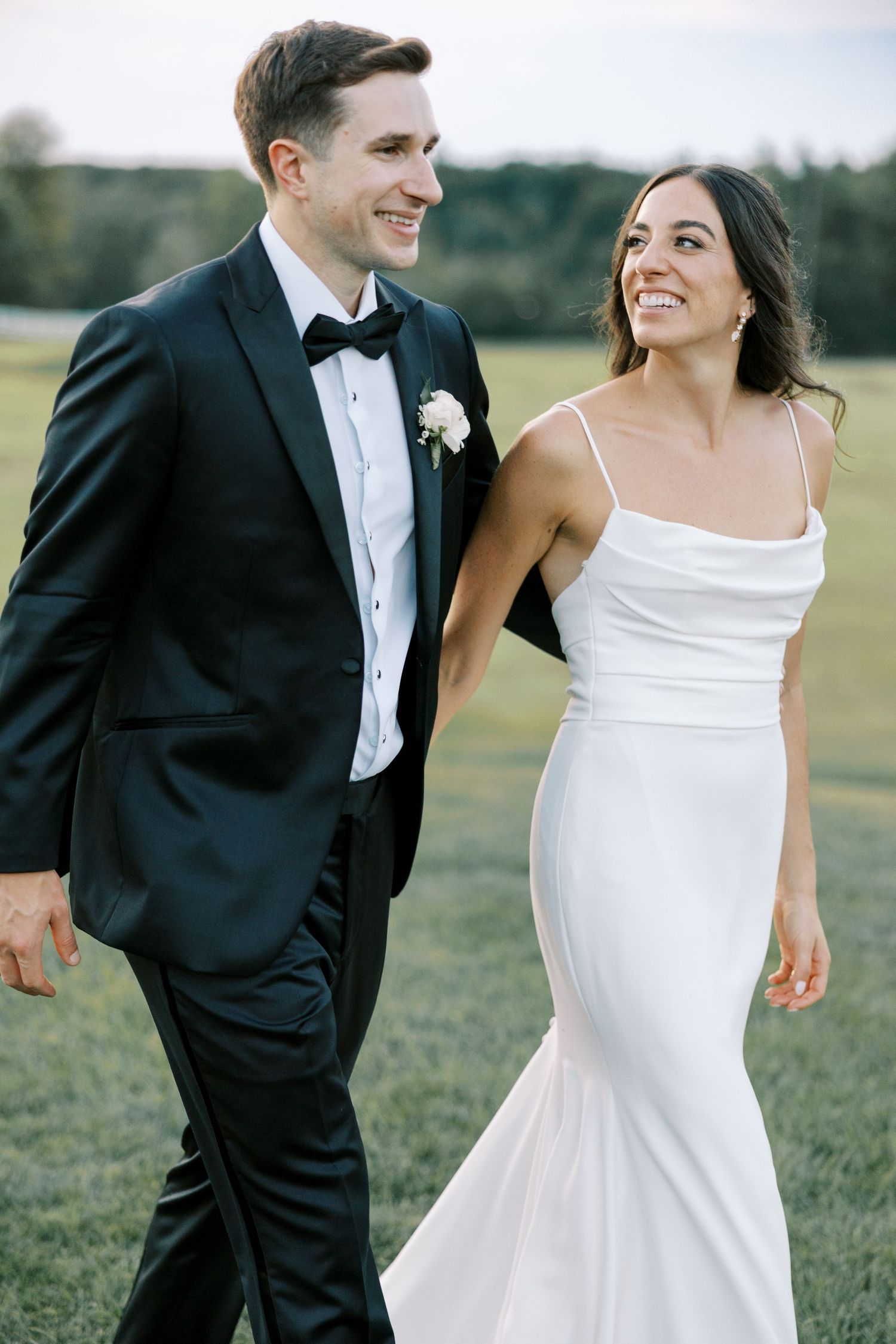 A couple in formal wedding attire shares playful moments in an outdoor field during their special day.