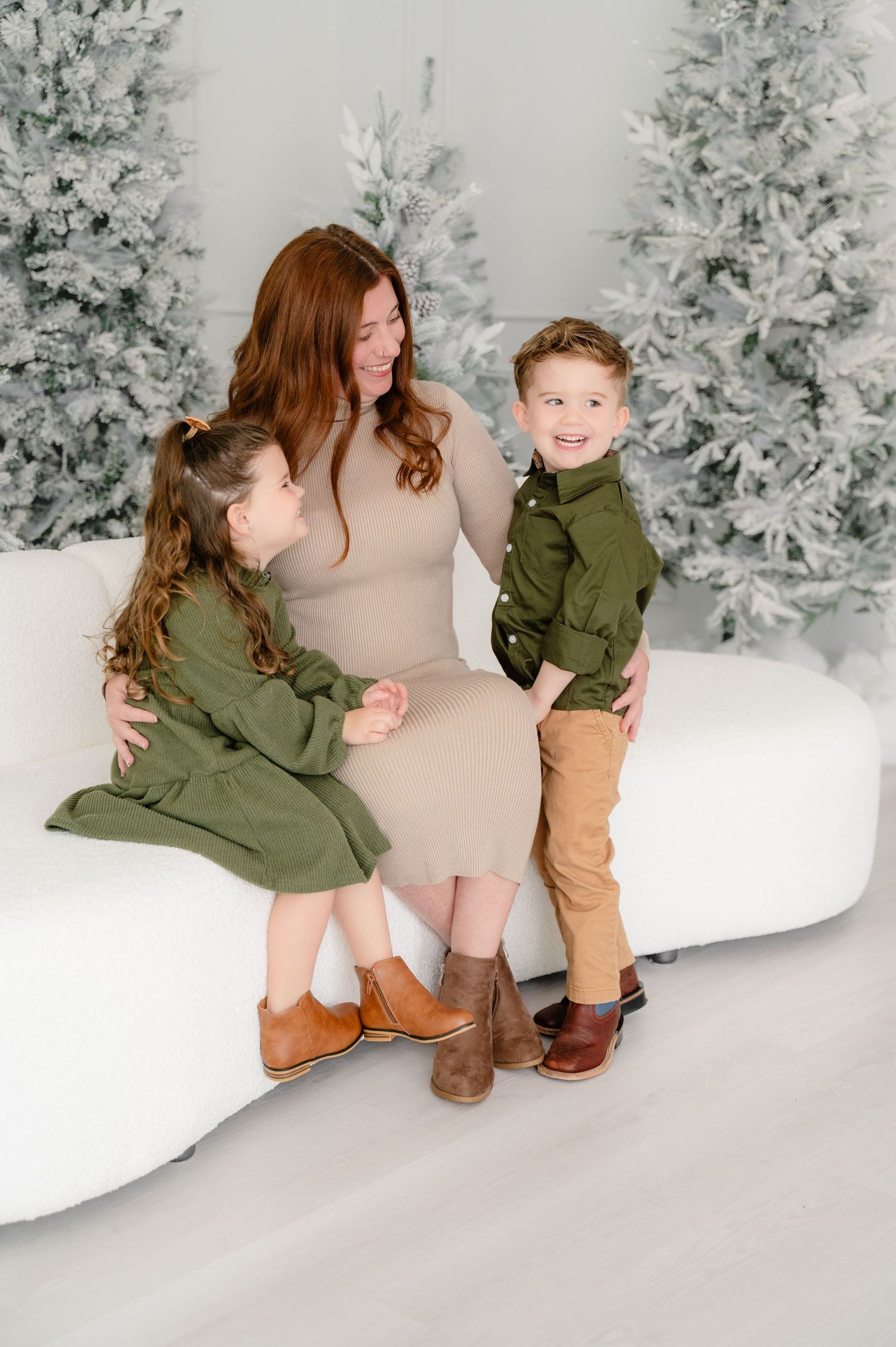 A heartwarming winter photo session with matching green and brown outfits against a snowy backdrop with frosted trees.