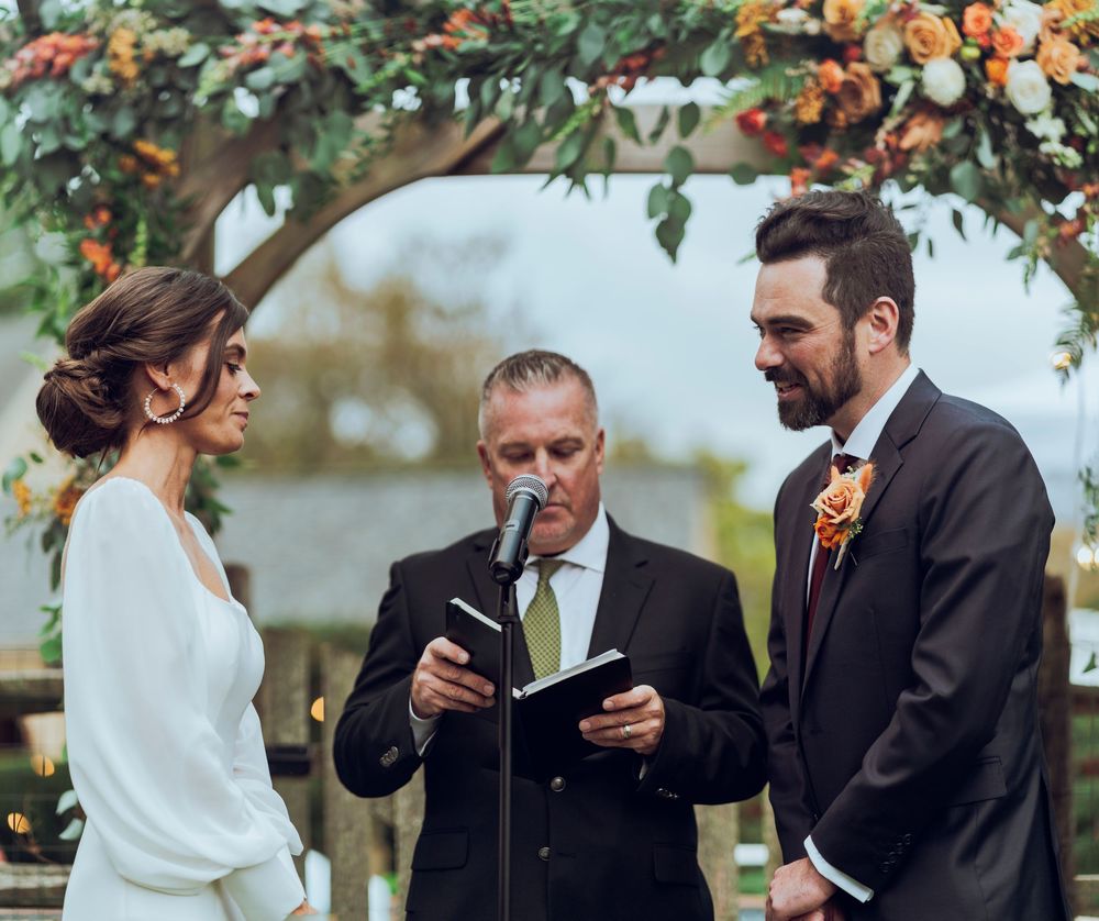 A man and a woman stand at the alter for their wedding surrounded by flowers
