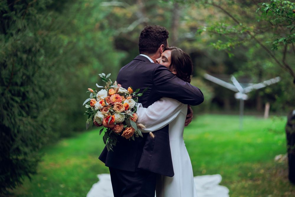 A couple hugs each other, one holding flowers, after their wedding ceremony