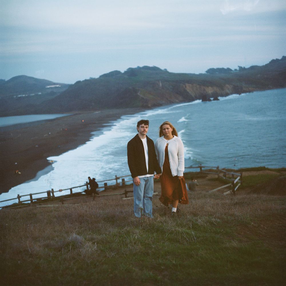 A couple poses holding each other's hand in front of a beautiful view of the ocean