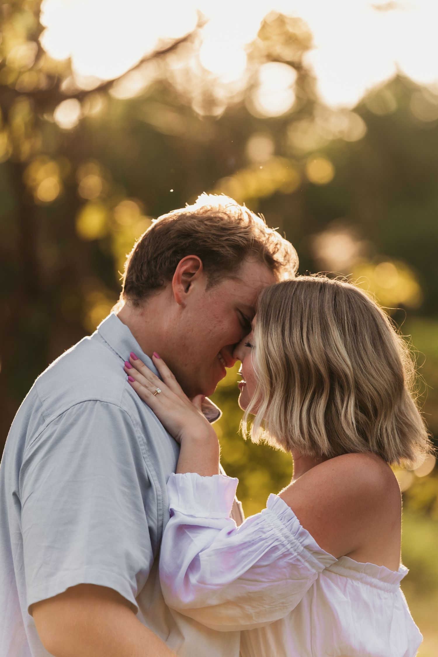 Intimate engagement photo of couple sharing tender moment in golden sunset light.
