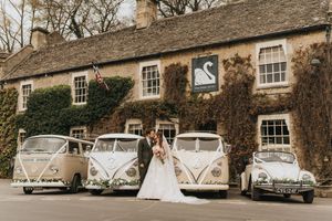 Three vintage Volkswagen vans and one classic car lined up in front of an ivy-covered stone cottage.