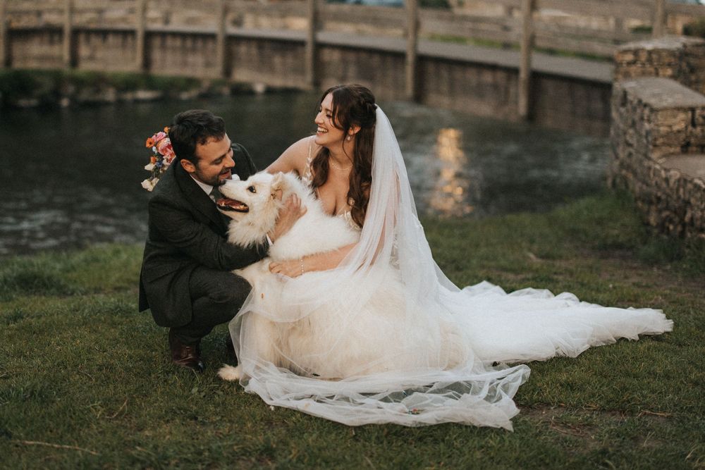 Two people share an intimate moment on grassy waterfront during sunset wedding photoshoot.