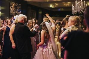 Guests dancing and celebrating at an elegant ballroom reception with chandelier lights overhead and formal evening attire.