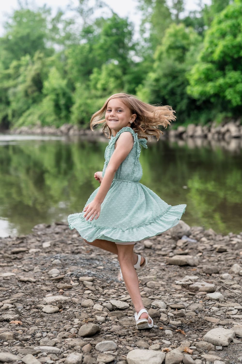 A sequence of four photos showing someone in a mint green dress twirling and dancing on rocky riverbank of Brecksville Reserve in Cleveland