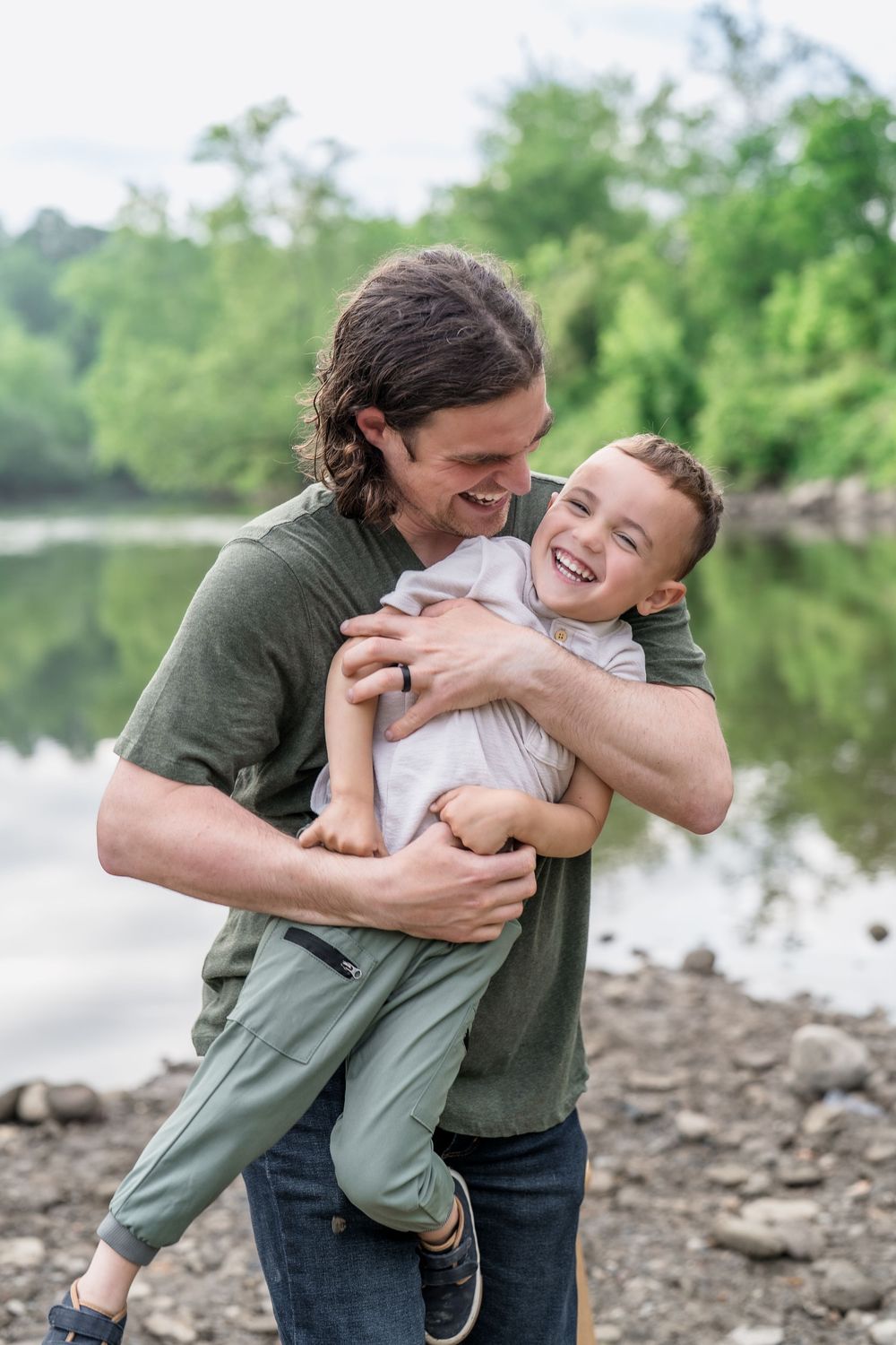 Parent and child share joyful embrace and laughter by riverside on rocky shore of Brecksville Reserve in Cleveland at a Family Photo Session