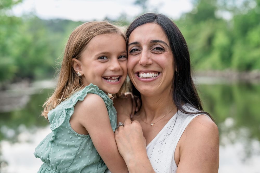 Two people sharing a joyful embrace outdoors against a lush green background with trees and water visible for Family Photo Session in Cle OH