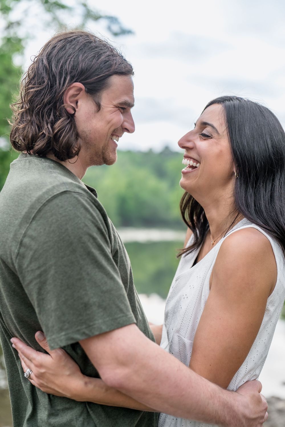 A couple embraces and laughs together outdoors on a summer day with a lake and trees in Brecksville Reserve in Cleveland, OH Family Photo