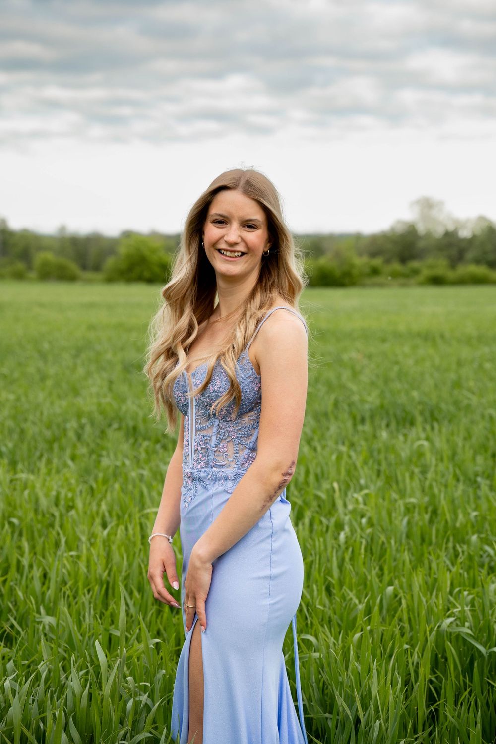 Elegant blue gown with embellished bodice photographed in a scenic green field during golden hour.