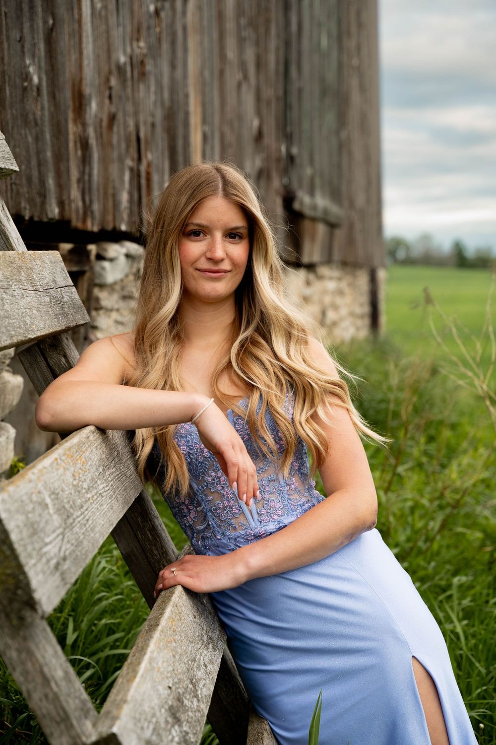 Elegant portrait next to a rustic wooden barn wearing a blue lace and satin formal dress.