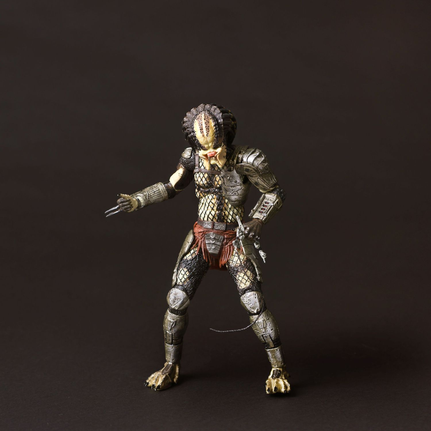A toy Predator action figure posed in a menacing stance against a dark background with dramatic lighting.