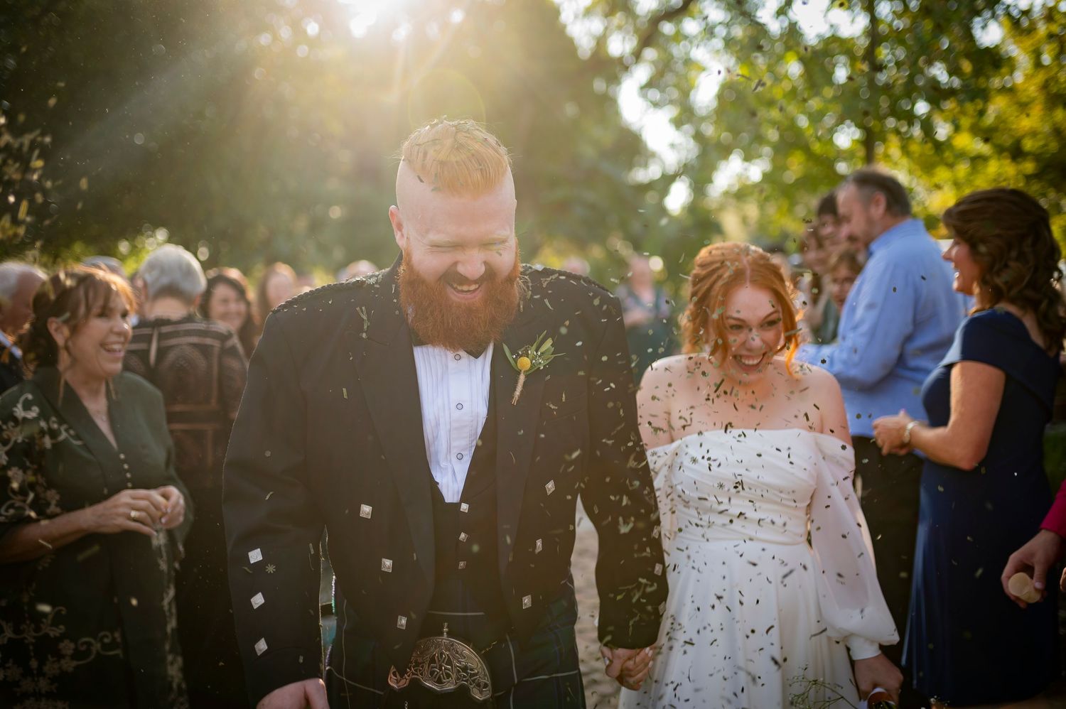 Wedding couple and guests share joyful moment with golden sun flare in outdoor celebration setting.