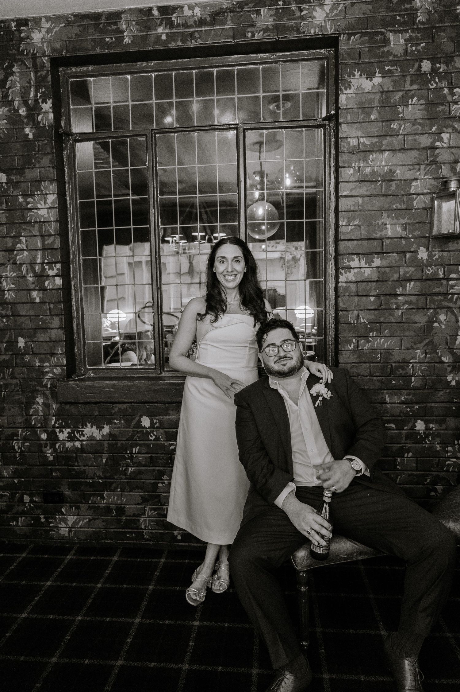 Black and white photo sequence showing playful poses against brick wall with window in creative engagement session.