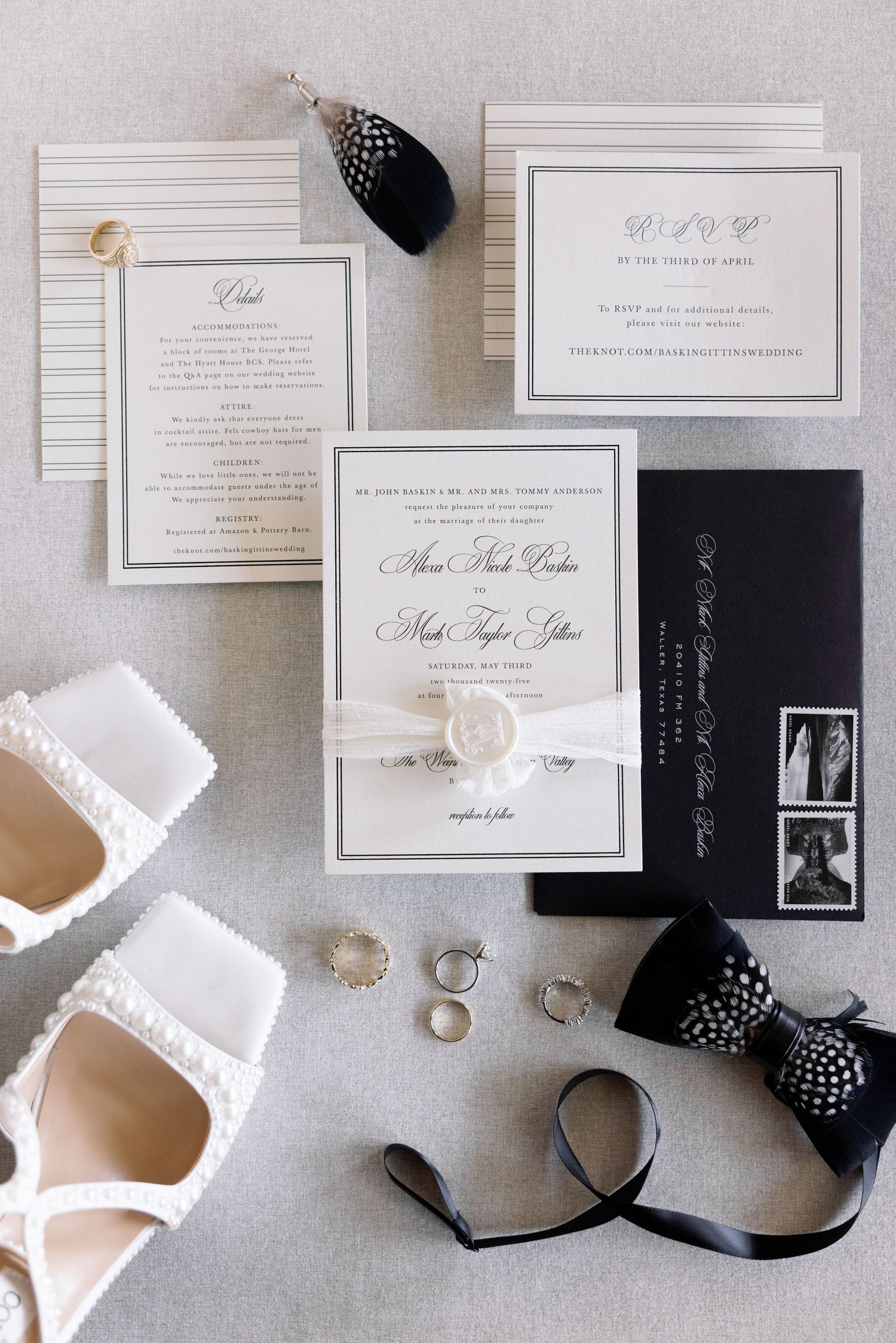 Black and white wedding stationery suite with invitation cards, rings, and silk ribbons laid flat on light gray surface.