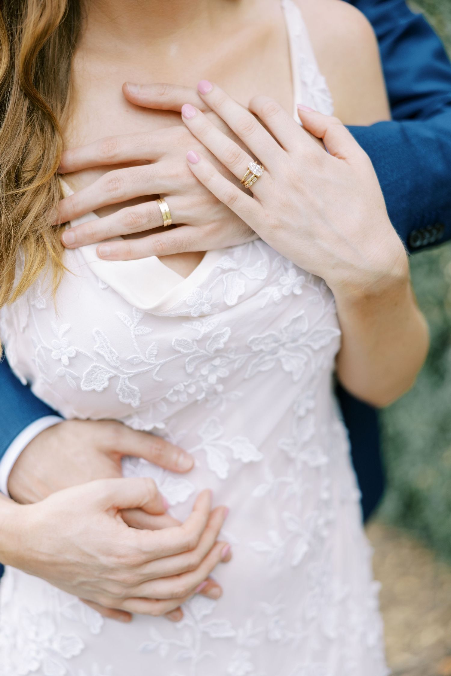 Close up of hands with engagement rings embracing against white lace wedding dress bodice at Ninety Acres.