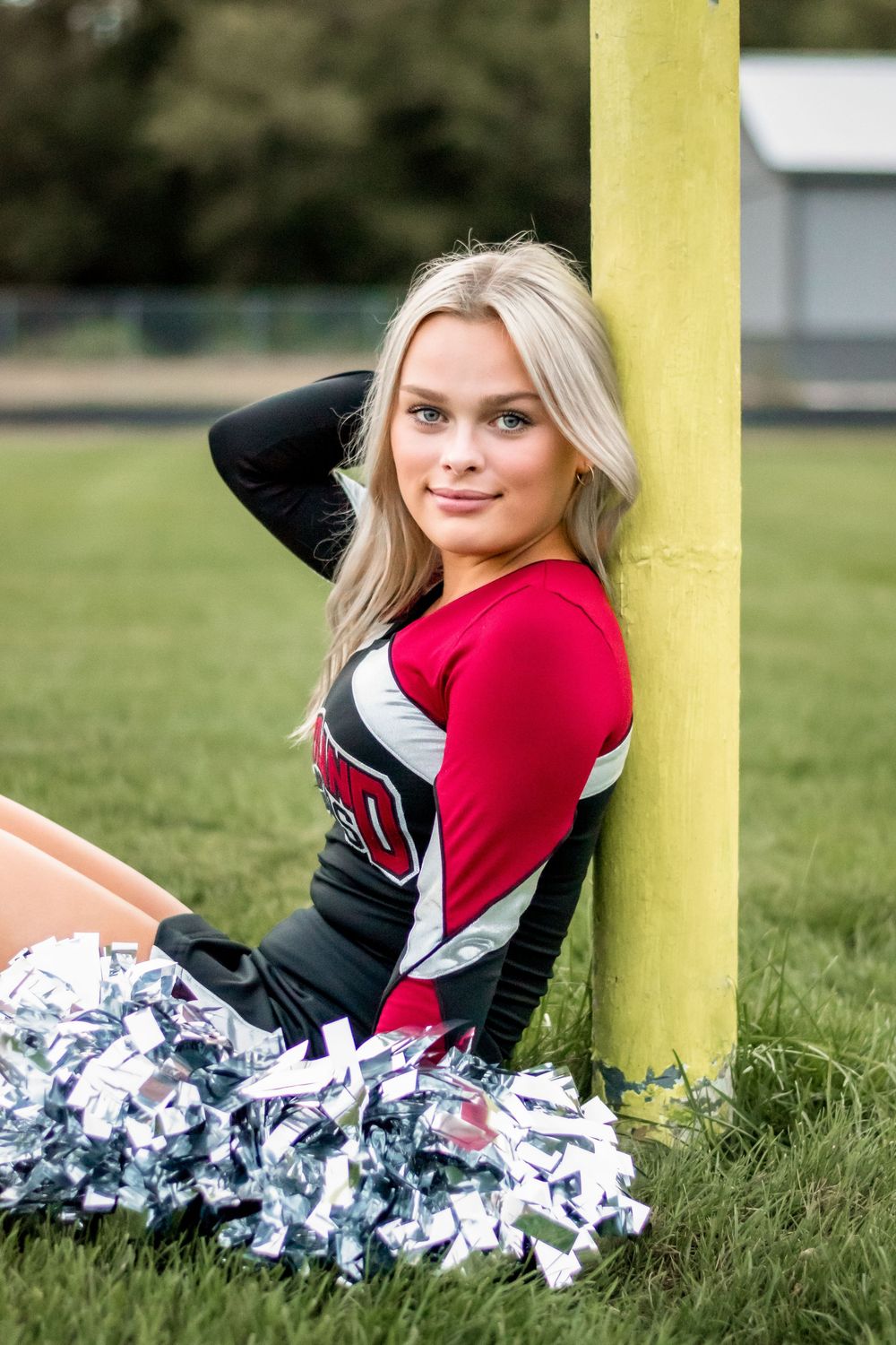 Portrait of a senior cheerleader leaning against a goalpost while in her cheer uniform.