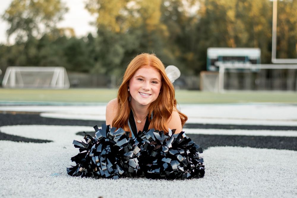 Senior cheerleader laying on field with pom poms in front during fun senior photo
