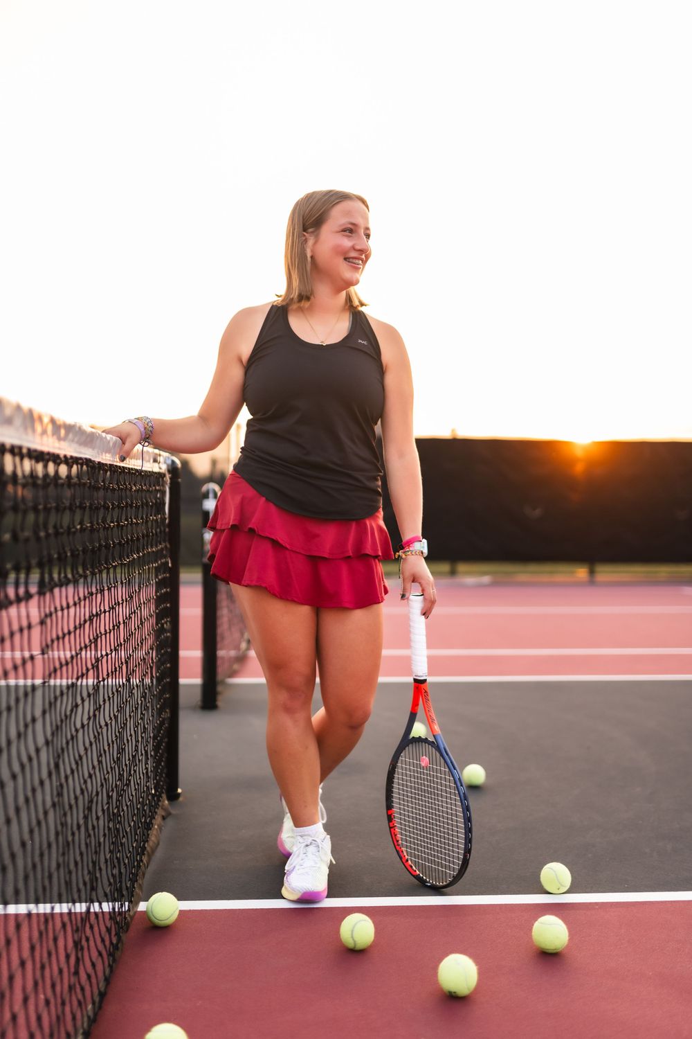 Portrait of a senior girl in her tennis uniform, with a tennis racket and tennis ball scattered on the court.