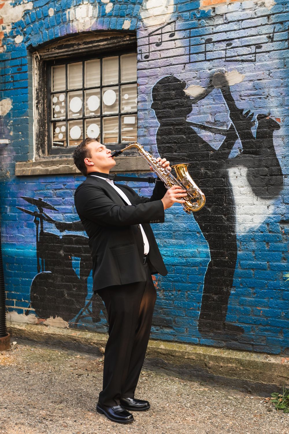 A senior portrait of a senior boy playing his saxophone, mimicking the saxophone mural in Old Town Lansing.