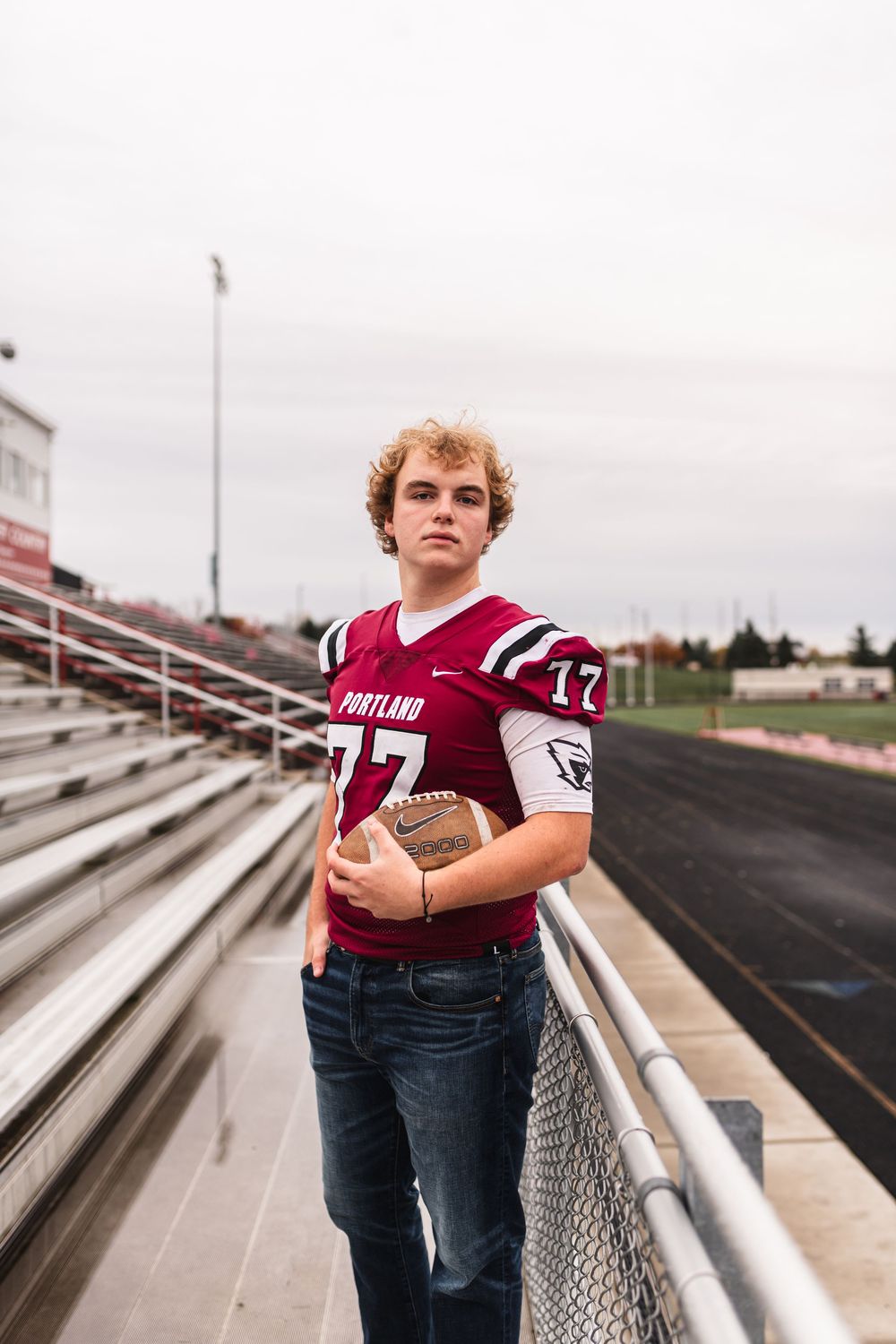 Senior boy holding football and wearing jersey on high school football field for senior portrait