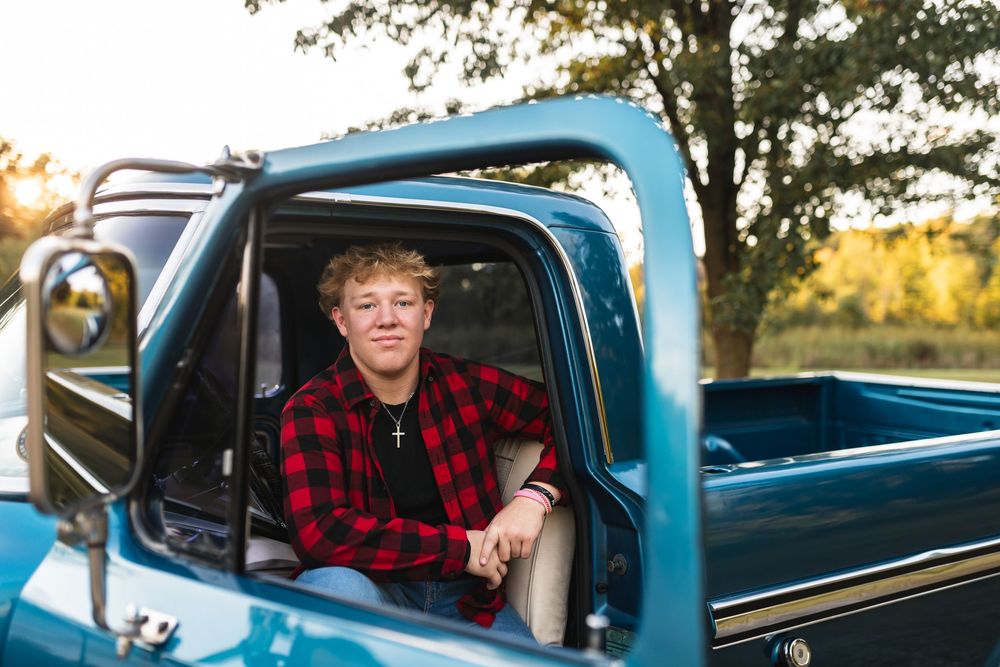 High school senior boy looking out window of vintage blue truck during classic car-themed session